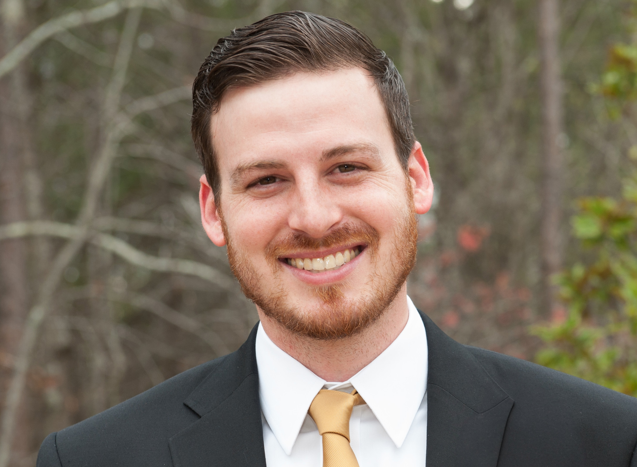 Travelers volunteer Nick Jones smiles wearing a black suit and gold tie.