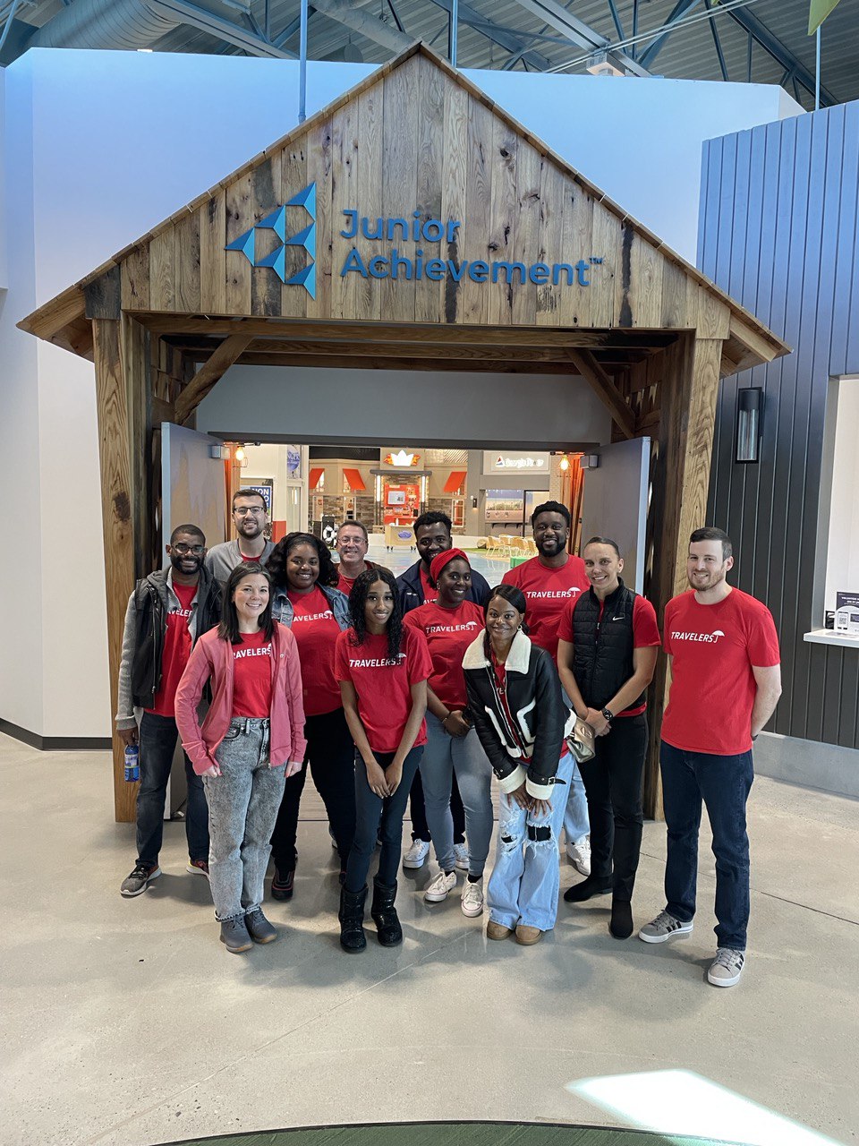 A group of Travelers employees in red Travelers shirts smiles for the camera at a Junior Achievement volunteer event.