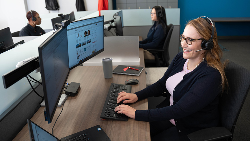 Smiling woman wearing a headset at her desk in a call center.