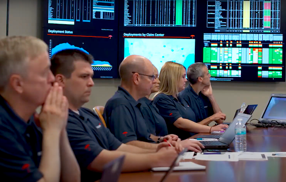 Travelers catastrophe response team seated at a conference table, reviewing data on large wall monitors displaying deployment and claims information.