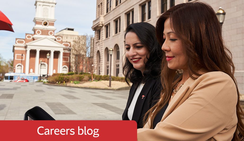 Two individuals in professional attire stand outdoors in a city setting. One wears a black outfit, the other a beige jacket. A historic building with columns and a clock tower is in the background. A red banner with 'Careers blog' is in the foreground.