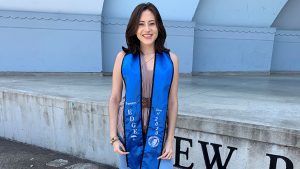 Diana Sanchez standing and smiling wearing a Travelers EDGE graduation sash.
