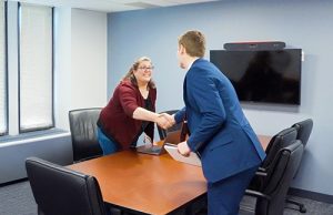 A person arriving at a job interview in a conference room and shaking the hand of another individual.