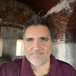 Person wearing a burgundy shirt standing inside a historic brick structure with arched ceiling.