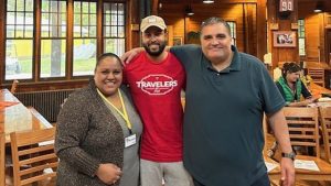 Interior of a rustic wooden camp with three people standing in the foreground.