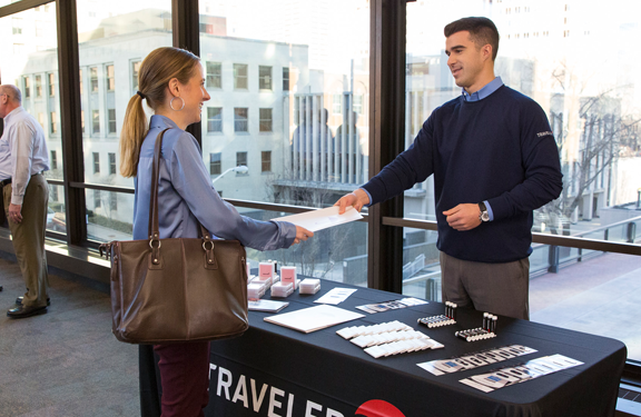 Travelers’ recruiter hands career information to a job seeker at a hiring event