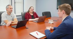 An individual being interviewed in a conference room by two other individuals.