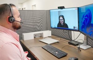 An individual sitting at a computer screen on a virtual call, talking to another individual.