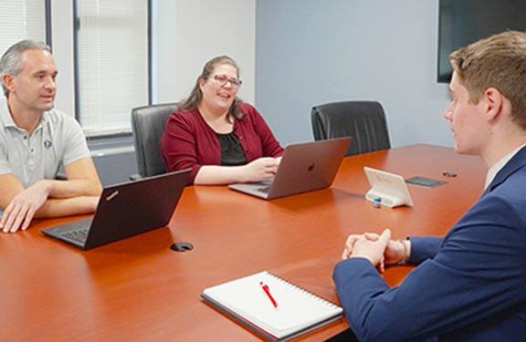 An individual being interviewed in a conference room by two other individuals.
