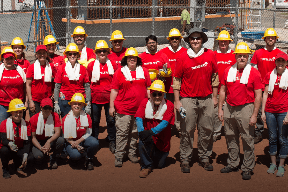 Cropped_Community-Involvement A group of people in red shirts and hard hats pose in front of a fenced area