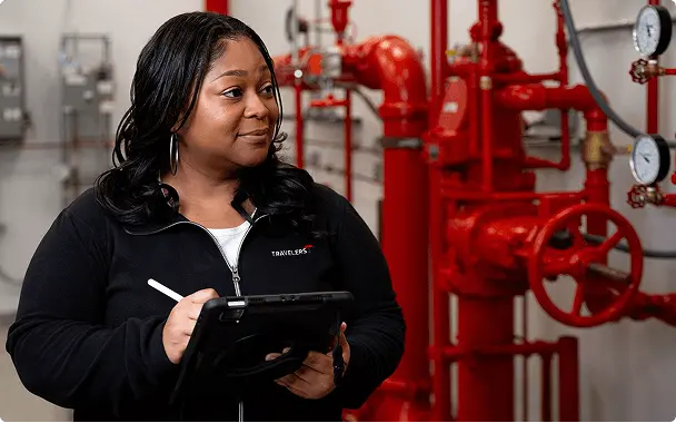A professional holding a tablet and writing tool inspecting a commercial fire sprinkler system.